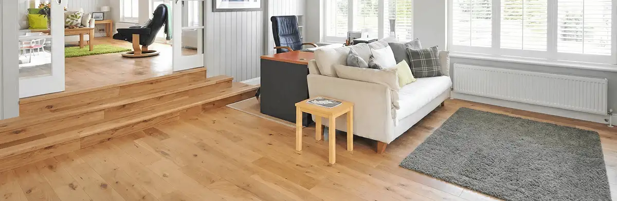 A modern living room with professionally installed laminate flooring, a beige sofa, a small side table, a gray rug, and large windows with white shutters in Tallahassee, FL